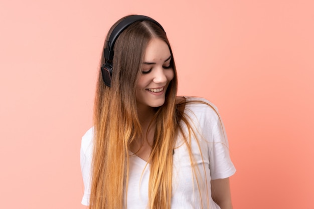 Jonge Kaukasische vrouw die op roze muur het luisteren muziek wordt geïsoleerd