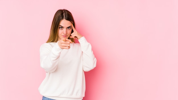 Jonge kaukasische vrouw die op roze muur tempel met vinger richt