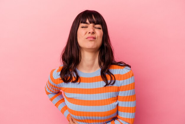 Jonge kaukasische vrouw die op roze muur wordt geïsoleerd die een leverpijn, buikpijn heeft.