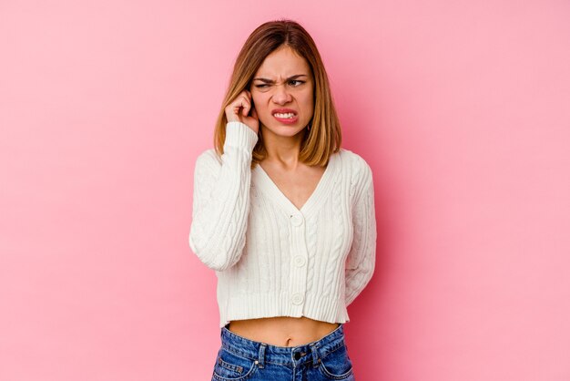 Jonge kaukasische vrouw die op roze muur wordt geïsoleerd die oren met handen behandelt