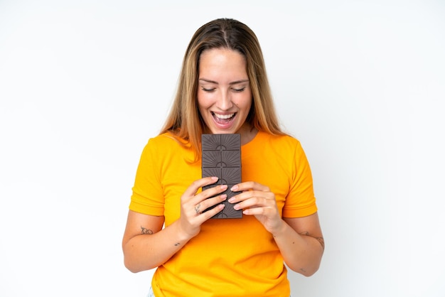 Jonge kaukasische vrouw die op witte achtergrond wordt geïsoleerd die een chocoladetablet eet