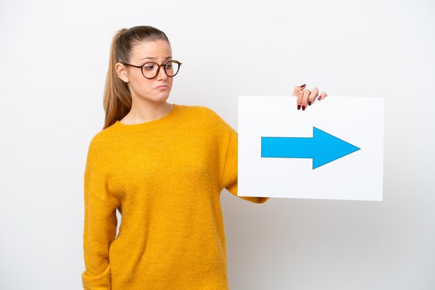 Jonge kaukasische vrouw die op witte achtergrond wordt geïsoleerd die een plakkaat met pijlsymbool houdt