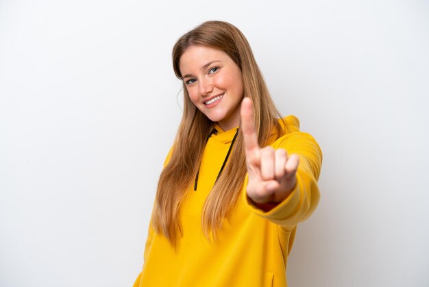 Jonge kaukasische vrouw die op witte achtergrond wordt geïsoleerd die een vinger toont en opheft