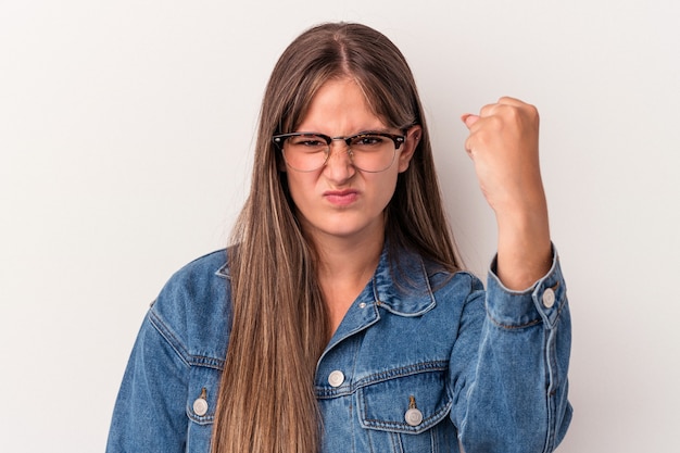 Jonge kaukasische vrouw die op witte achtergrond wordt geïsoleerd die vuist toont aan camera, agressieve gezichtsuitdrukking.