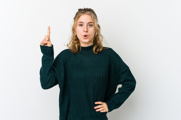 Jonge kaukasische vrouw die op witte muur met geopende mond wijst.