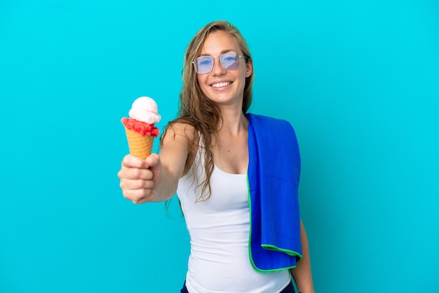 Jonge kaukasische vrouw die roomijs houdt en een strandhanddoek draagt die op blauwe achtergrond met gelukkige uitdrukking wordt geïsoleerd