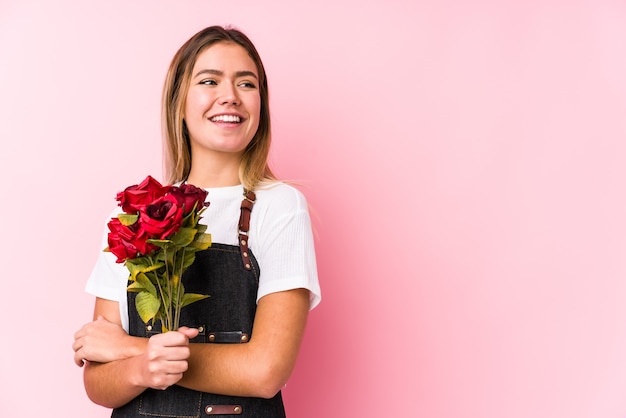 Jonge kaukasische vrouw die rozen geïsoleerd glimlachend zelfverzekerd met gekruiste armen houdt.