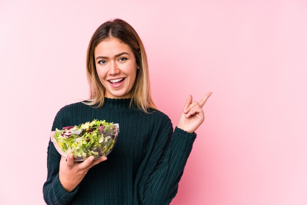 Jonge Kaukasische vrouw die salade het glimlachen houden die vrolijk met weg wijsvinger richten.