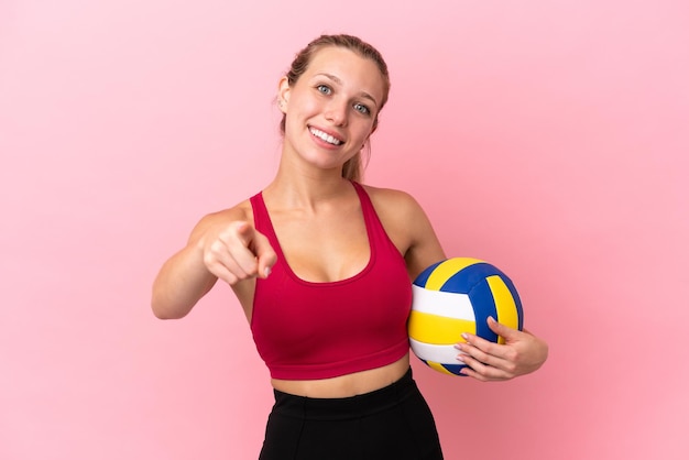 Jonge kaukasische vrouw die volleybal speelt geïsoleerd op een roze achtergrond die naar voren wijst met een gelukkige uitdrukking