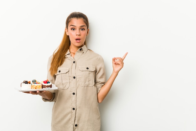 Jonge Kaukasische vrouw die zoete cakes houdt die aan de kant richten