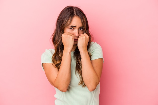 Jonge kaukasische vrouw geïsoleerd op roze achtergrond die een vuistslag gooit, woede, vecht vanwege een ruzie, boksen.