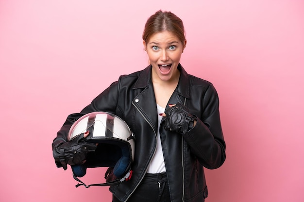 Jonge kaukasische vrouw met een motorhelm die op roze achtergrond met verrassingsgelaatsuitdrukking wordt geïsoleerd