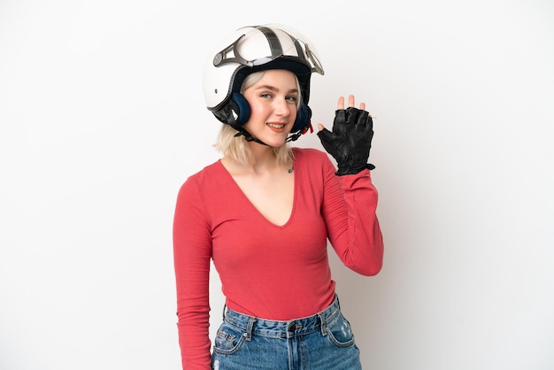 Jonge kaukasische vrouw met een motorhelm die op witte achtergrond wordt geïsoleerd die met hand met gelukkige uitdrukking salueert