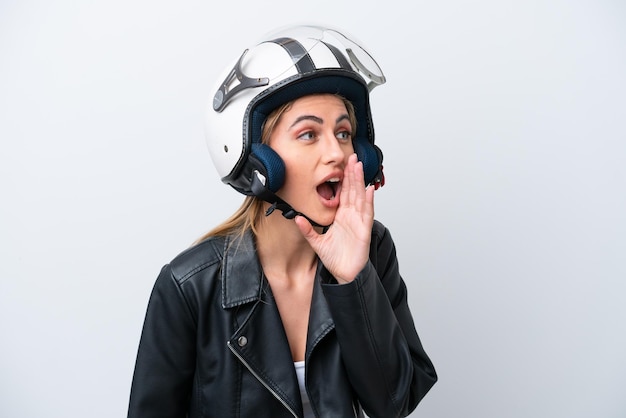 Jonge kaukasische vrouw met een motorhelm die op witte achtergrond wordt geïsoleerd en met wijd open mond naar de zijkant schreeuwt