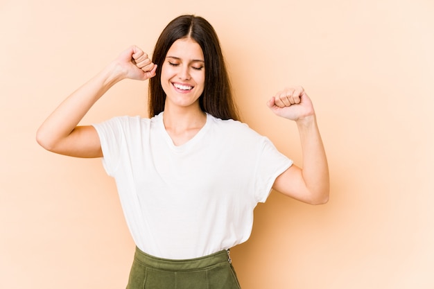 Jonge Kaukasische vrouw op beige muur dansen en plezier maken.