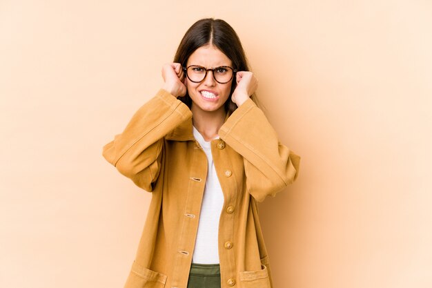 Jonge Kaukasische vrouw op beige muur die oren behandelen met handen.