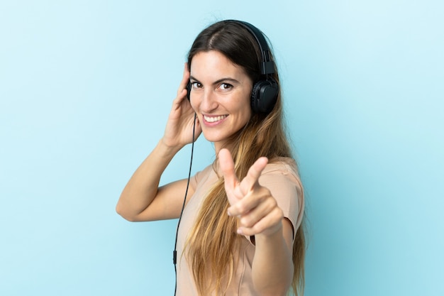 Jonge Kaukasische vrouw op blauwe muur het luisteren muziek en het richten aan de voorzijde