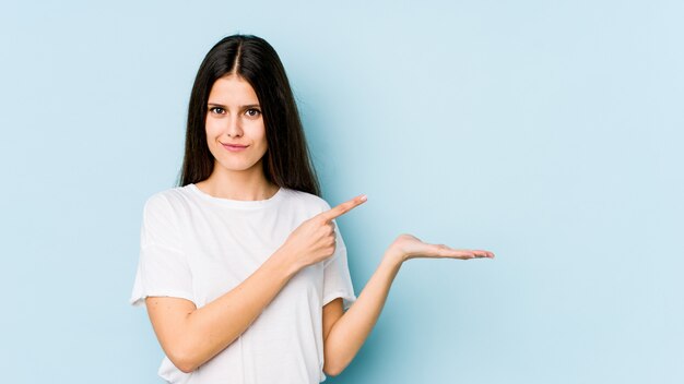 Jonge Kaukasische vrouw op blauwe opgewekte muur houdend een lege ruimte op palm.