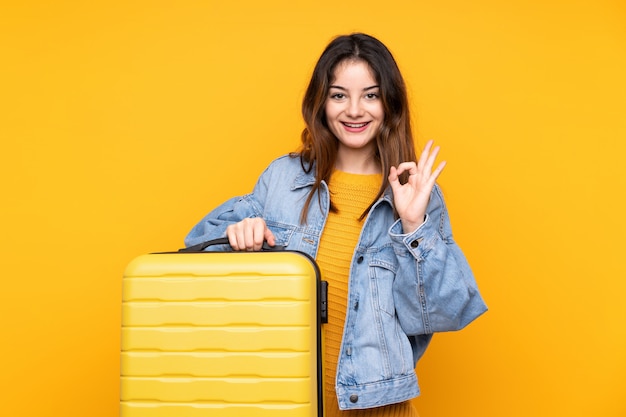 Jonge Kaukasische vrouw op gele muur in vakantie met reiskoffer
