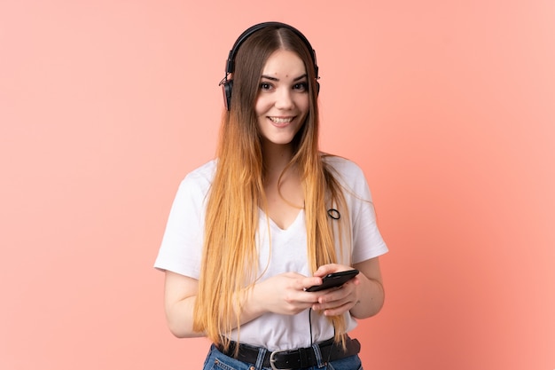 Jonge Kaukasische vrouw op roze muur het luisteren muziek met mobiel en het kijken voorzijde