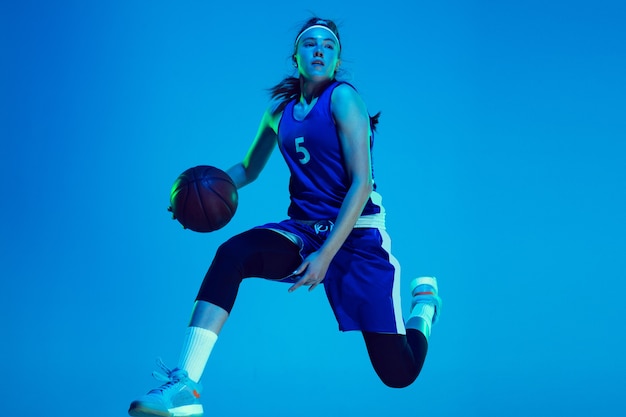 Jonge kaukasische vrouwelijke basketbalspeler die op blauwe studioachtergrond in neonlicht wordt geïsoleerd