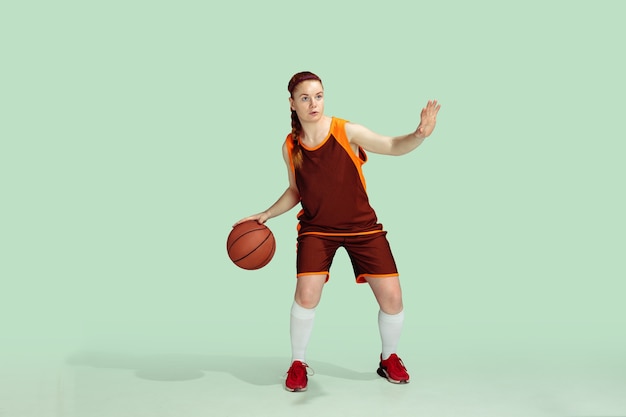 Jonge Kaukasische vrouwelijke basketbalspeler in actie, beweging tijdens gameplay geïsoleerd op mint gekleurde achtergrond. Concept van sport, beweging, energie en dynamische, gezonde levensstijl. Trainen, oefenen.