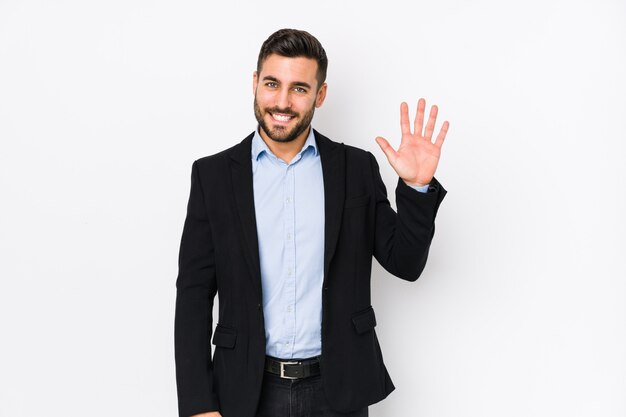 Jonge Kaukasische zakenman tegen een witte muur die vrolijk tonend nummer vijf met vingers glimlacht.