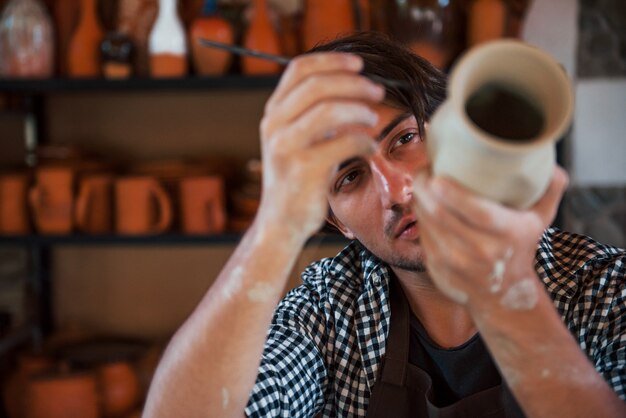 Jonge keramist houdt zijn verse handgemaakte pot vast en maakt wat detaillering met een speciaal gereedschapsstokje.