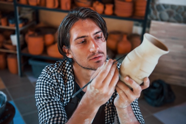 Jonge keramist houdt zijn verse handgemaakte pot vast en maakt wat detaillering met een speciaal gereedschapsstokje.