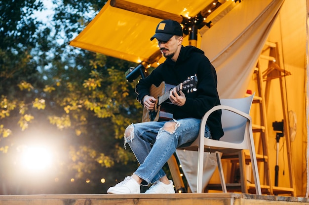 Jonge kerel die 's avonds akoestische gitaar speelt in de natuur