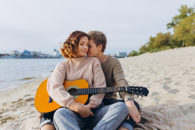 Jonge kerel leert zijn vriendin gitaar spelen autodidact Verliefd stel dat plezier heeft op het strand, knuffelt en zoent