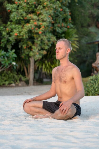 Jonge kerel met dreadlocks doet yoga op een tropisch strand, close-up. Het concept van een gezonde levensstijl