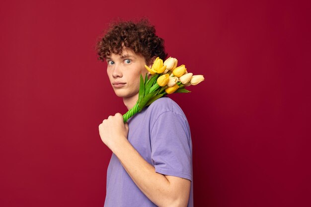 Jonge kerel met een geel boeket bloemen paarse t-shirts rode achtergrond ongewijzigd