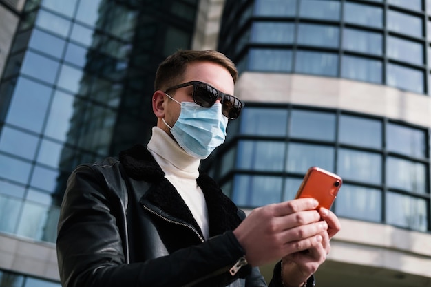 Jonge kerel met een medisch masker gebruikt een telefoon op straat, quarantaineconcept