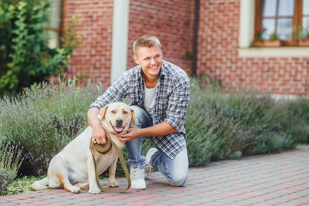 Foto jonge kerel met retriever op wandeling in zomerpark. knappe man met zijn hond golden retriever buitenshuis.