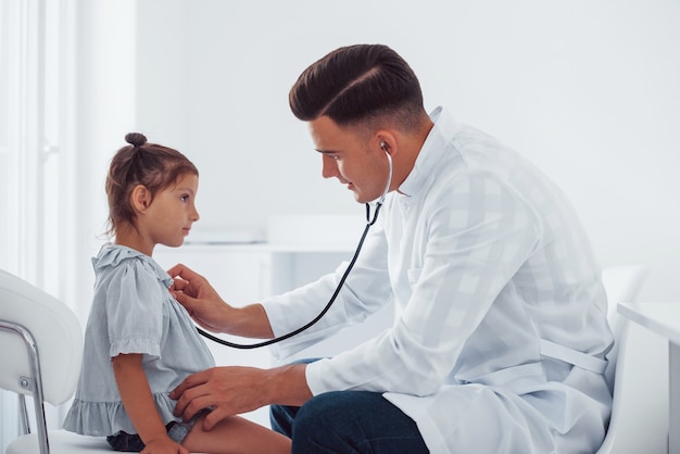 Jonge kinderarts werkt met kleine vrouwelijke bezoeker in de kliniek.