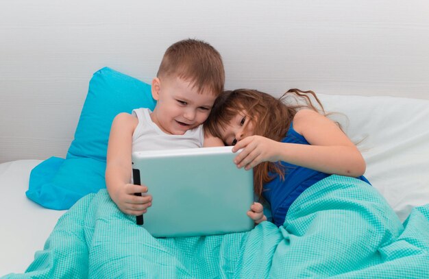 Jonge kinderen genieten van digitale gadget in de slaapkamer van het huis. Kinderen liggen op bed en spelen op tablet. Onderwijstechnologie van het leren van concept van vrije tijd. Een kind met gadget.