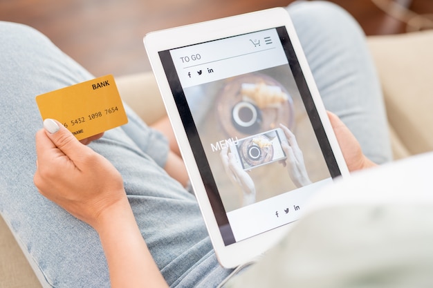 Jonge klant met creditcard en touchpad tijdens het bladeren door goederen in de online winkel