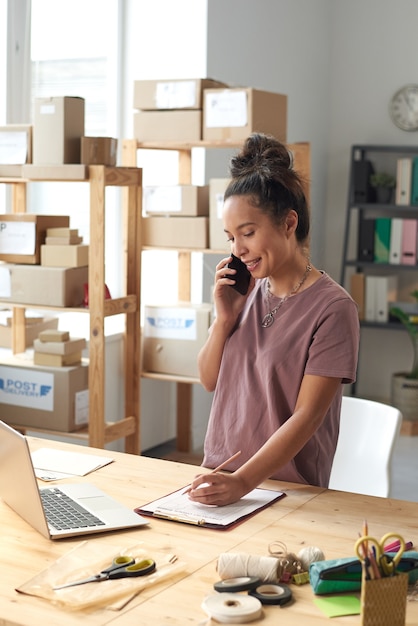 Jonge kleermaker die een bestelling neemt tijdens haar gesprek op de mobiele telefoon op kantoor