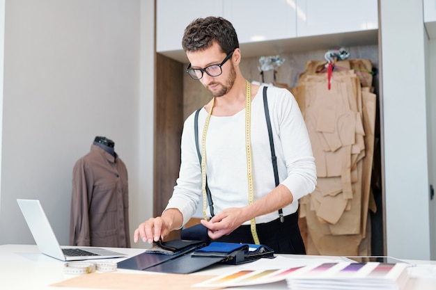 Jonge kleermaker in vrijetijdskleding die door textielmonsters kijkt terwijl hij aan zijn nieuwe modecollectie werkt