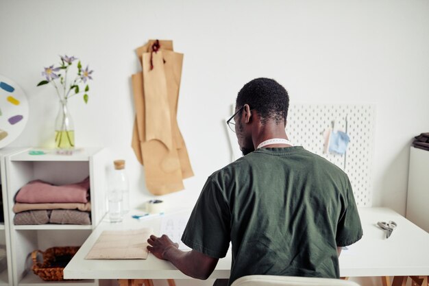 Jonge kleermaker zit aan een bureau in zijn studio en kiest een naaipatroon voor zijn volgende project