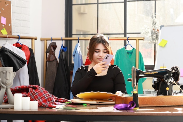 Jonge kleermaker zit aan het bureau en neemt foto met haar telefoon