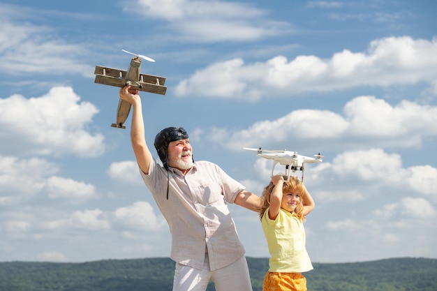 Jonge kleinzoon en oude grootvader met vliegtuig en quadcopter drone over blauwe lucht en wolken achtergrond...