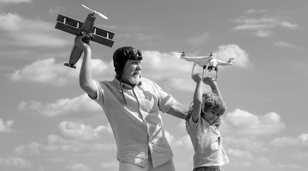 Jonge kleinzoon en oude grootvader met vliegtuig en quadcopter drone over blauwe lucht en wolken backgrou