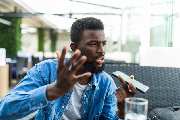 Jonge knappe Afrikaanse man boos praten telefoon op luidspreker in café