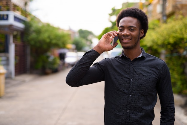 Jonge knappe Afrikaanse man met behulp van mobiele telefoon buitenshuis