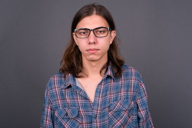 Jonge knappe androgyne hipster man met lang haar tegen grijze muur