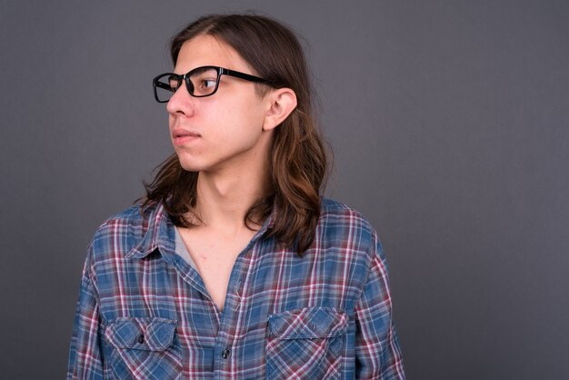 Jonge knappe androgyne hipster man met lang haar tegen grijze muur