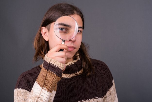 jonge knappe androgyne man met lang haar klaar voor de winter tegen grijze muur