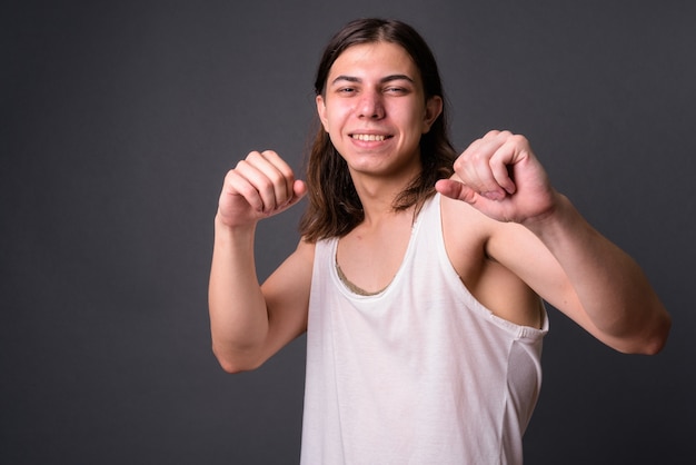 Jonge knappe androgyne man met lang haar tegen grijze muur